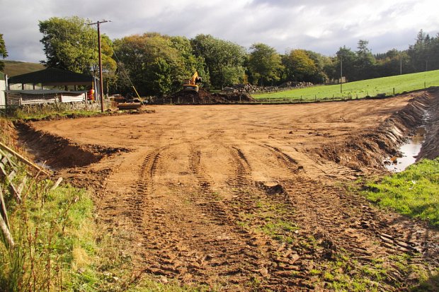New drain passing under a field access with heap of topsoil being tidied in the background